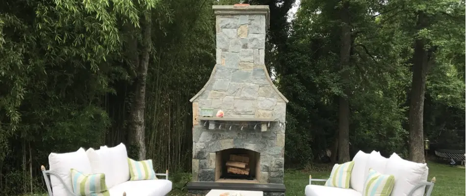 A stone outdoor fireplace in Chevy Chase, MD, surrounded by trees and white couches.