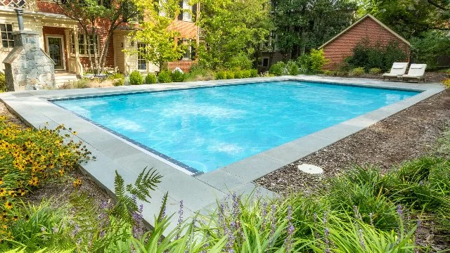 A pool in an outdoor space surrounded by landscaping.